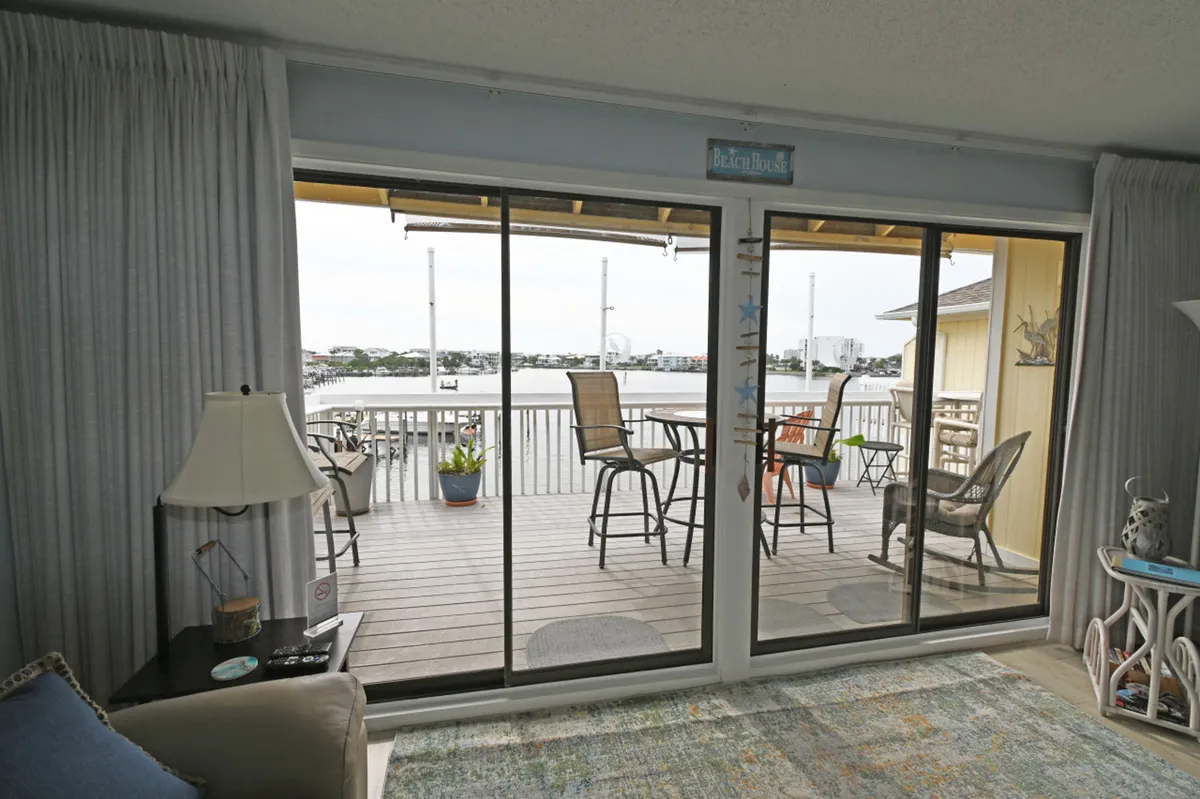 This image features large sliding glass doors opening to a spacious balcony with an inviting outdoor seating area, all set against a beautiful harbor view. Coastal decor accents reinforce a sense of place, while the arrangement invites relaxation, morning coffee, or unwinding with a drink at sunset.