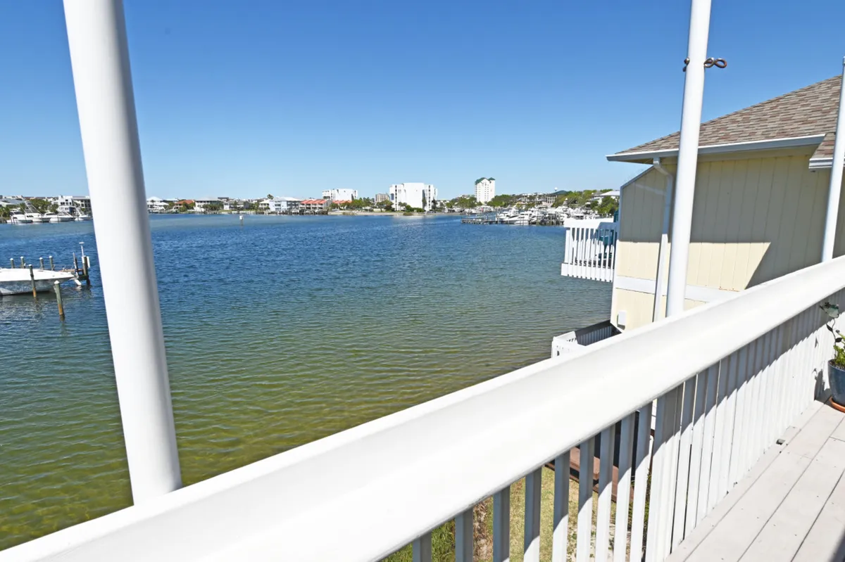 A tranquil view from the private deck, showcasing white railings, calm harbor waters with boats, and neighboring buildings. The serene setting invites guests to relax, enjoy coffee, or watch sunsets over the marina.