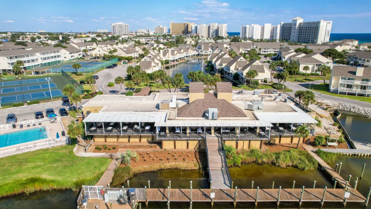 A sweeping view of the resort's main clubhouse, covered patio, boat docks, tennis courts, multiple swimming pools, and landscaped grounds. The image conveys a vibrant yet relaxing atmosphere, with options for recreation and leisure.