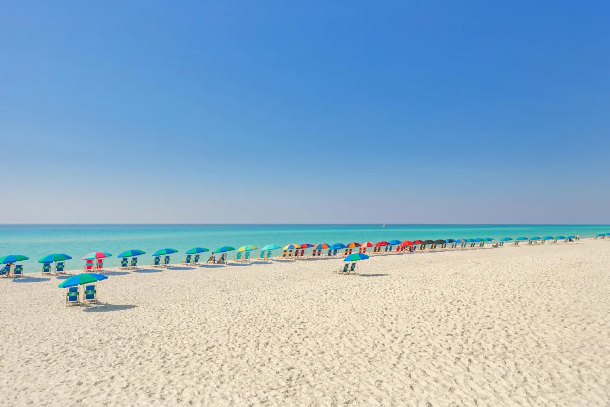 A picture-perfect view of a row of colorful beach umbrellas on a spotless white sandy beach, with calm turquoise ocean water and a clear blue sky stretching overhead. The image is free of crowds, focusing on the serenity and rejuvenating atmosphere of the beach experience.